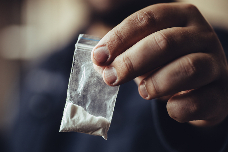 close up of hand holding a small plastic packet containing white powdered substance