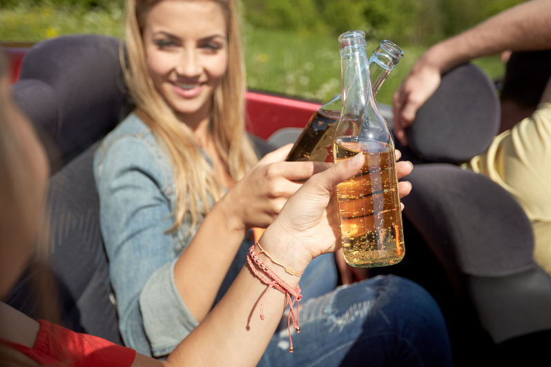 Happy teens having a beer in a vehicle while driving.