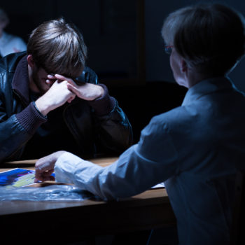 Man being interrogated by a female officer in dark room after a drug search.