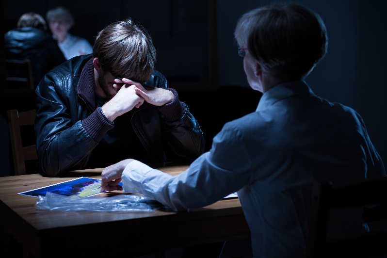 Man being interrogated by a female officer in dark room after a drug search.