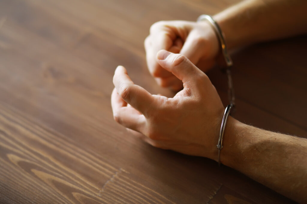 Close-up of Hands in Handcuffs on Wooden Table - Concept of Law Enforcement and Justice