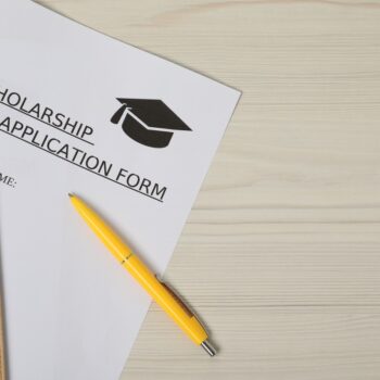 Scholarship application form and pen on wooden table, flat lay. Space for text