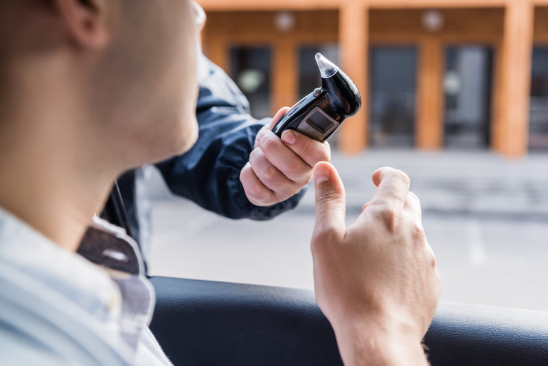 cropped view of policeman giving breathalyzer to driver in car, blurred foreground,stock image