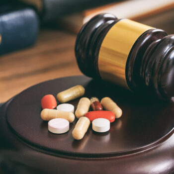 Law gavel and colorful pills on a wooden desk, dark background